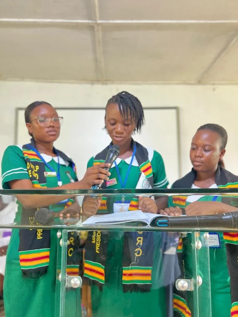 Female student in green nursing uniform presenting citation award to woman in white dress during handover ceremony